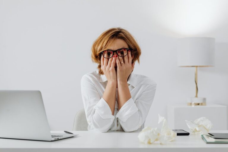 Femme les mains sur le visage à son bureau, ordinateur portable et mouchoirs