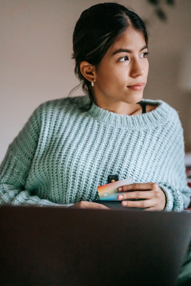 Jeune femme tenant une carte de débit devant son ordinateur portable