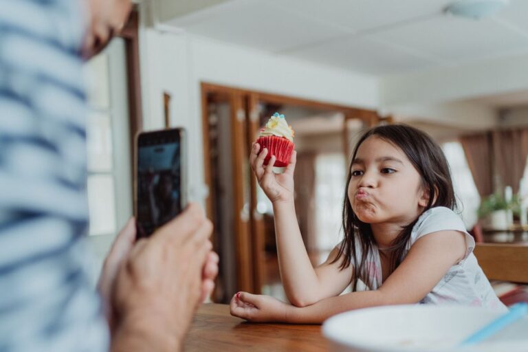 Père photographiant sa fille tenant un petit gâteau