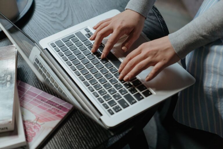 Mains d'une femme tapant sur un ordinateur portable, entourée de livres